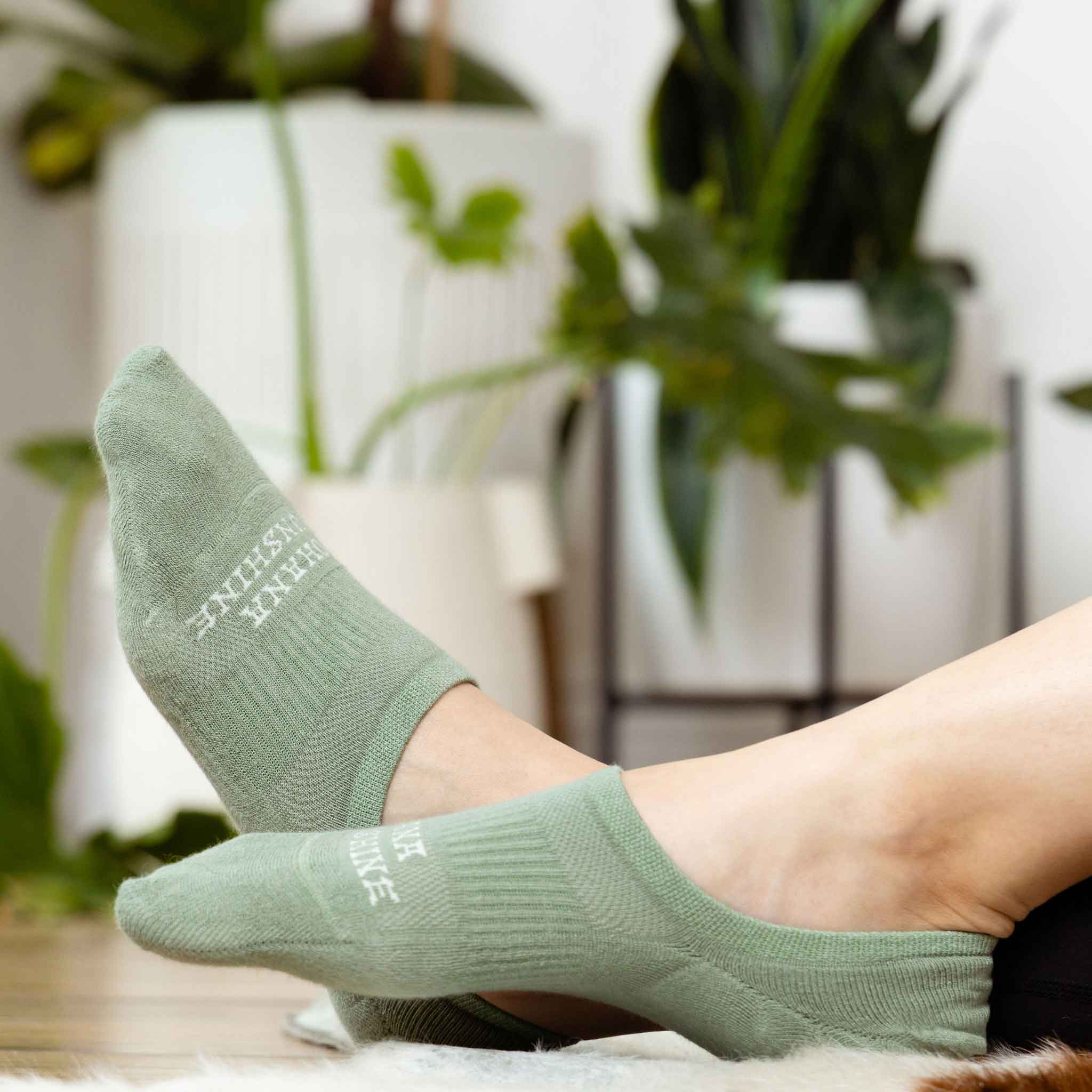 Relaxed view of feet wearing green no-show socks by Ohana Sunshine, with indoor plants in the background for a cozy lifestyle setting