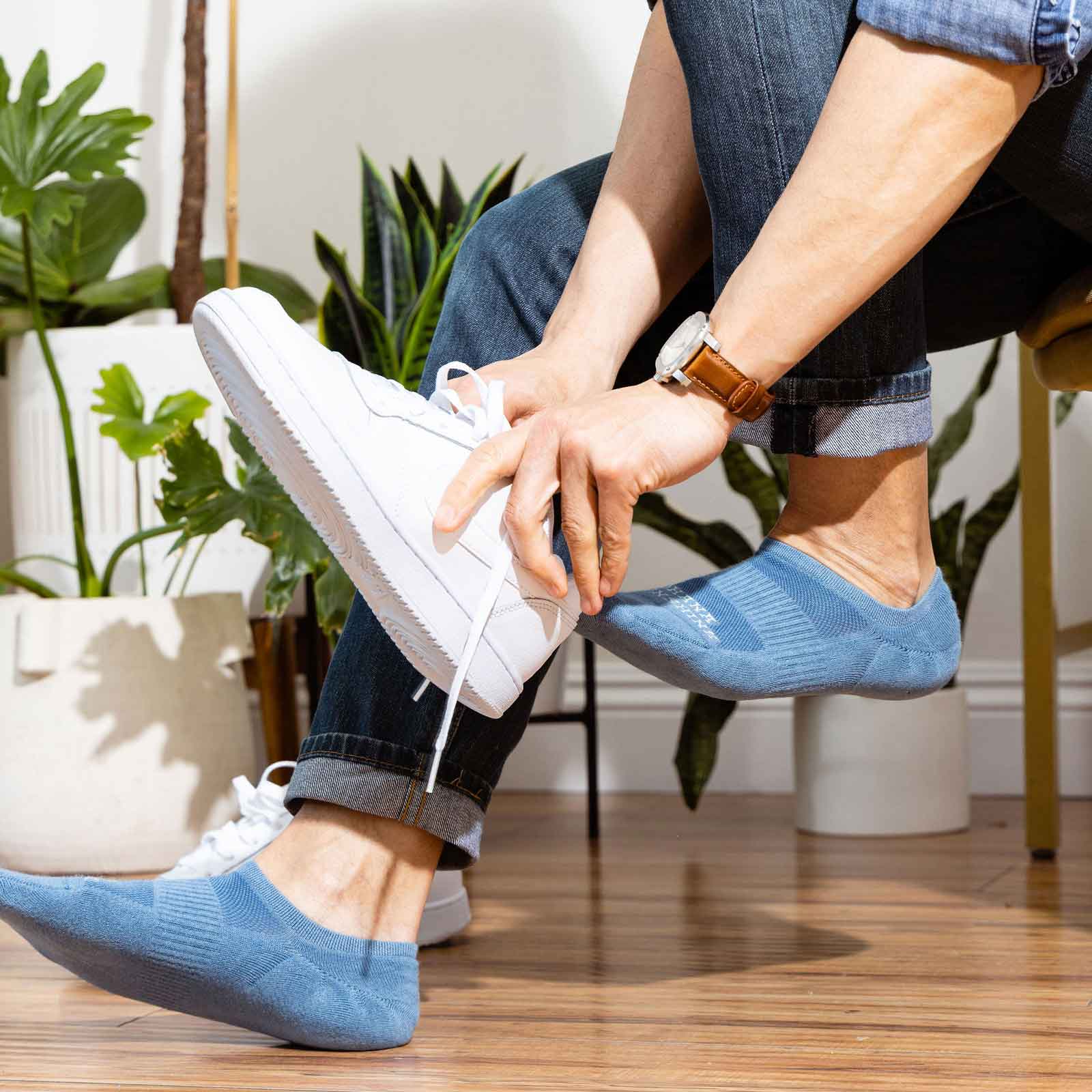 An image of a male model's feet with blue no show socks, paired with white shoes. The socks are barely visible, but provide a comfortable and stylish layer between the feet and the shoes. The model's toes are slightly visible and the socks sit perfectly on his feet, allowing for a clean and polished look. 