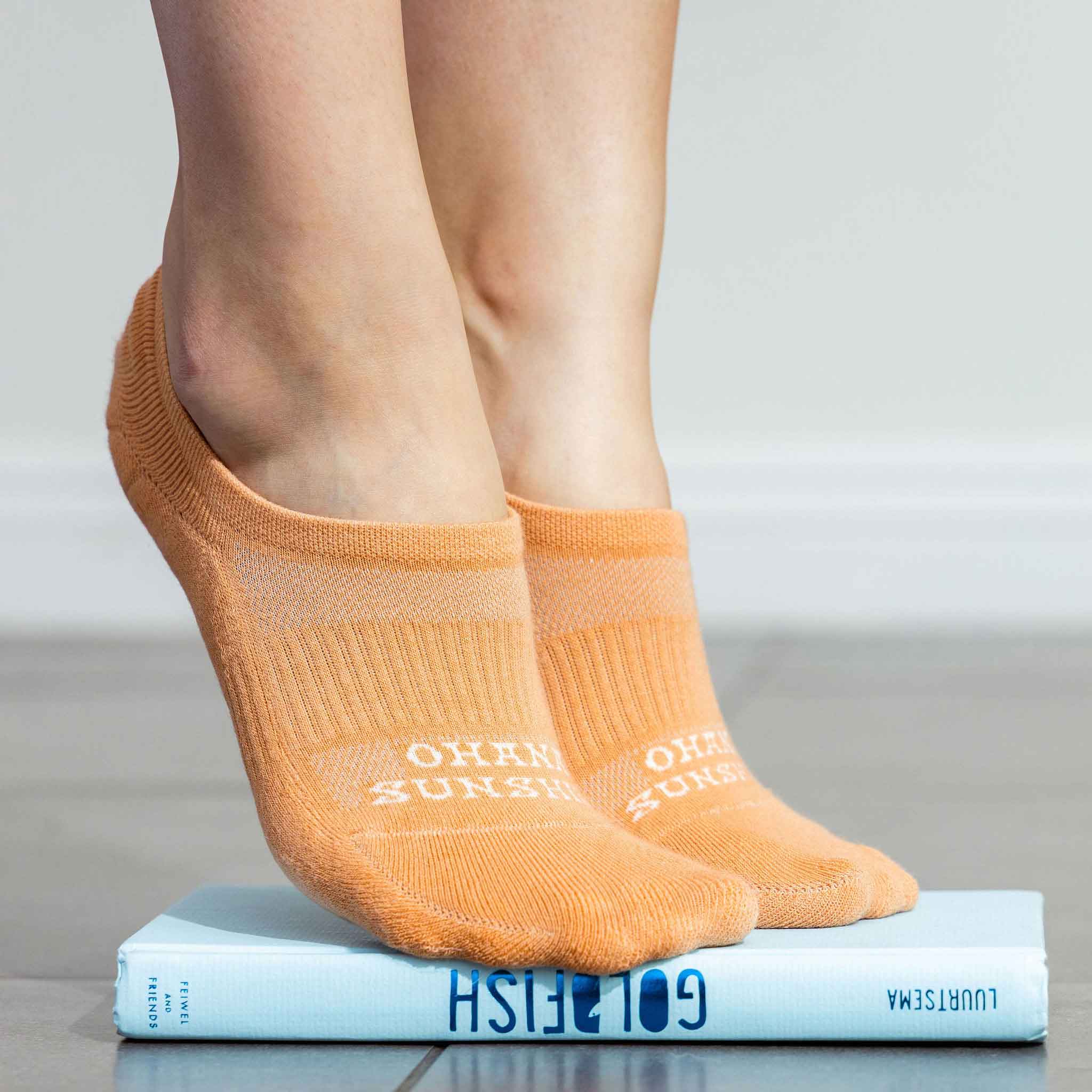 Model wearing orange no-show socks by Ohana Sunshine, highlighting the snug, low-cut fit and  seamless toes in a stretching tip toes pose